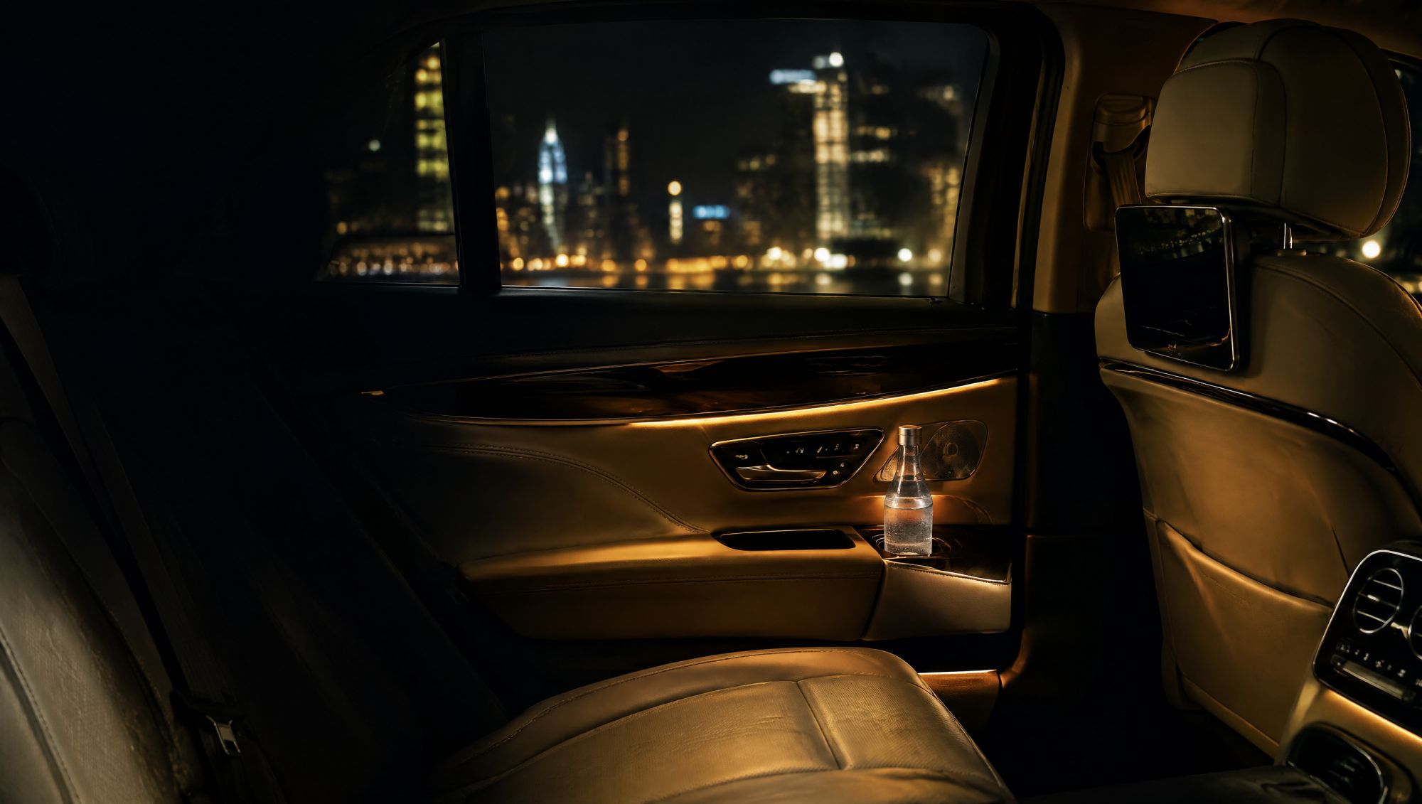 Rear leather seat of a chauffeured car at night with warm gold lighting